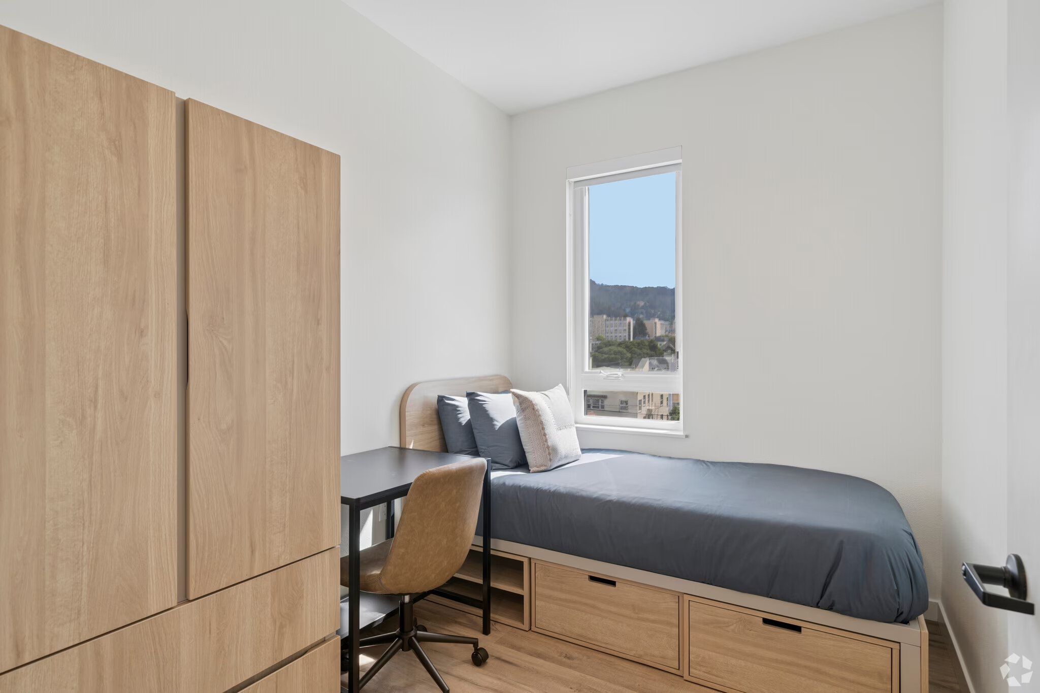 Fully furnished apartment bedroom featuring a bed, a dedicated desk area, and large window at ArtHaus Dwight in Berkeley, CA.