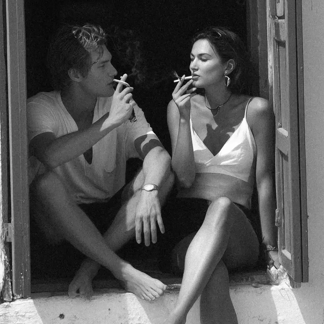 Couple sur le rebord d'une fenêtre fumant une cigarette