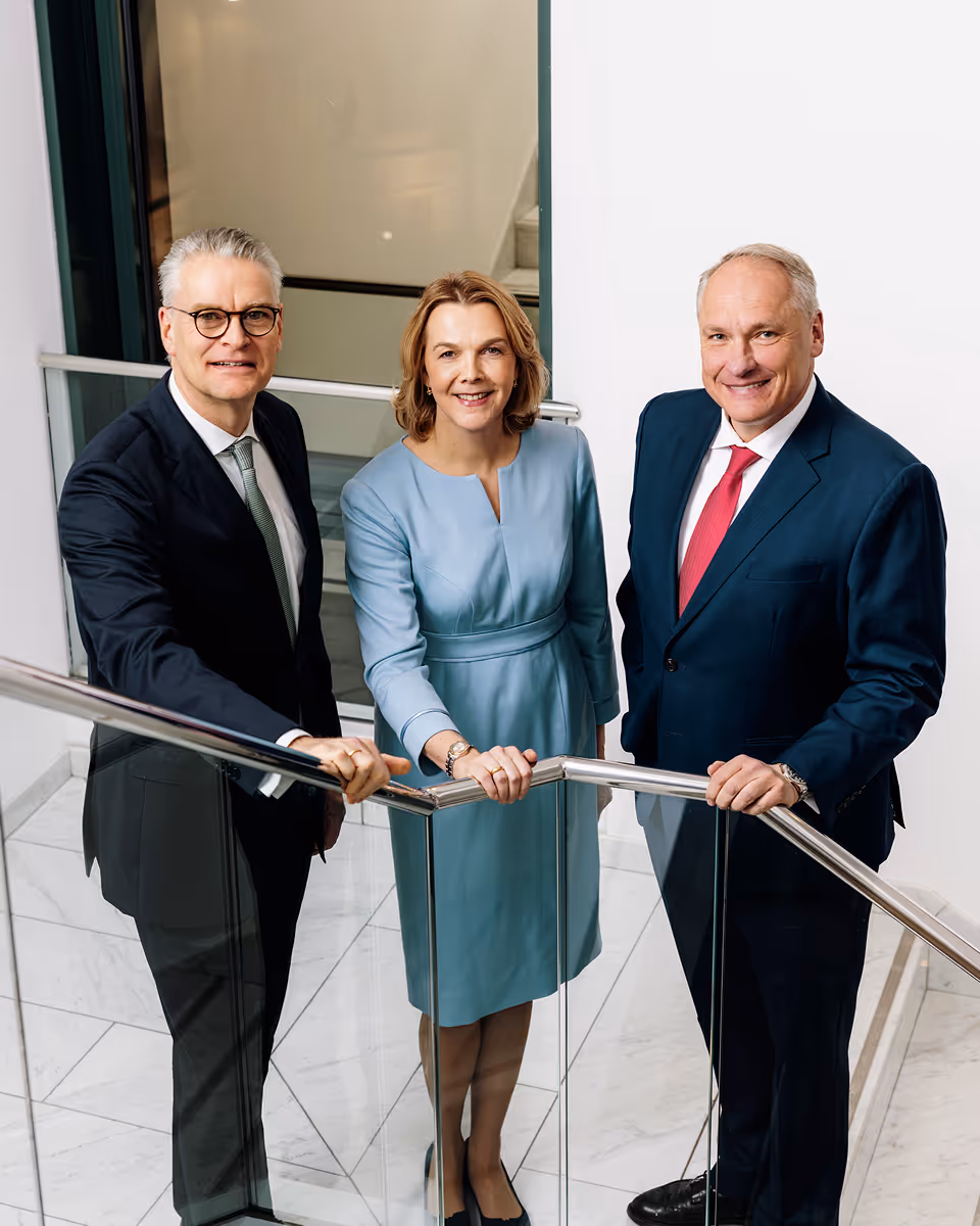 Drei Führungskräfte, 2 Männer eine Frau, stehen im Treppenhaus und blicken in die Kamera.
