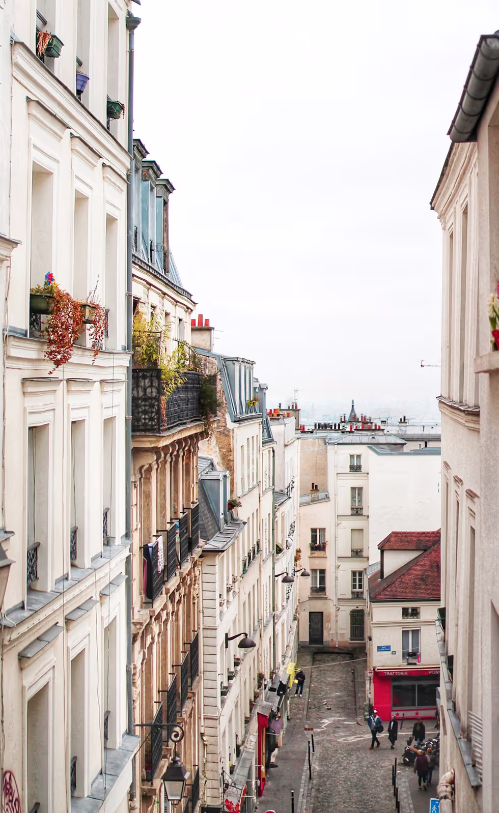 Vue d'une rue parisienne charmante avec des bâtiments anciens, des balcons fleuris et des passants.