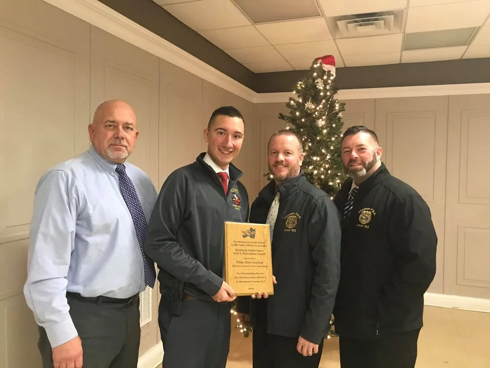 Four men standing indoors in front of a decorated Christmas tree, one holding a plaque award.