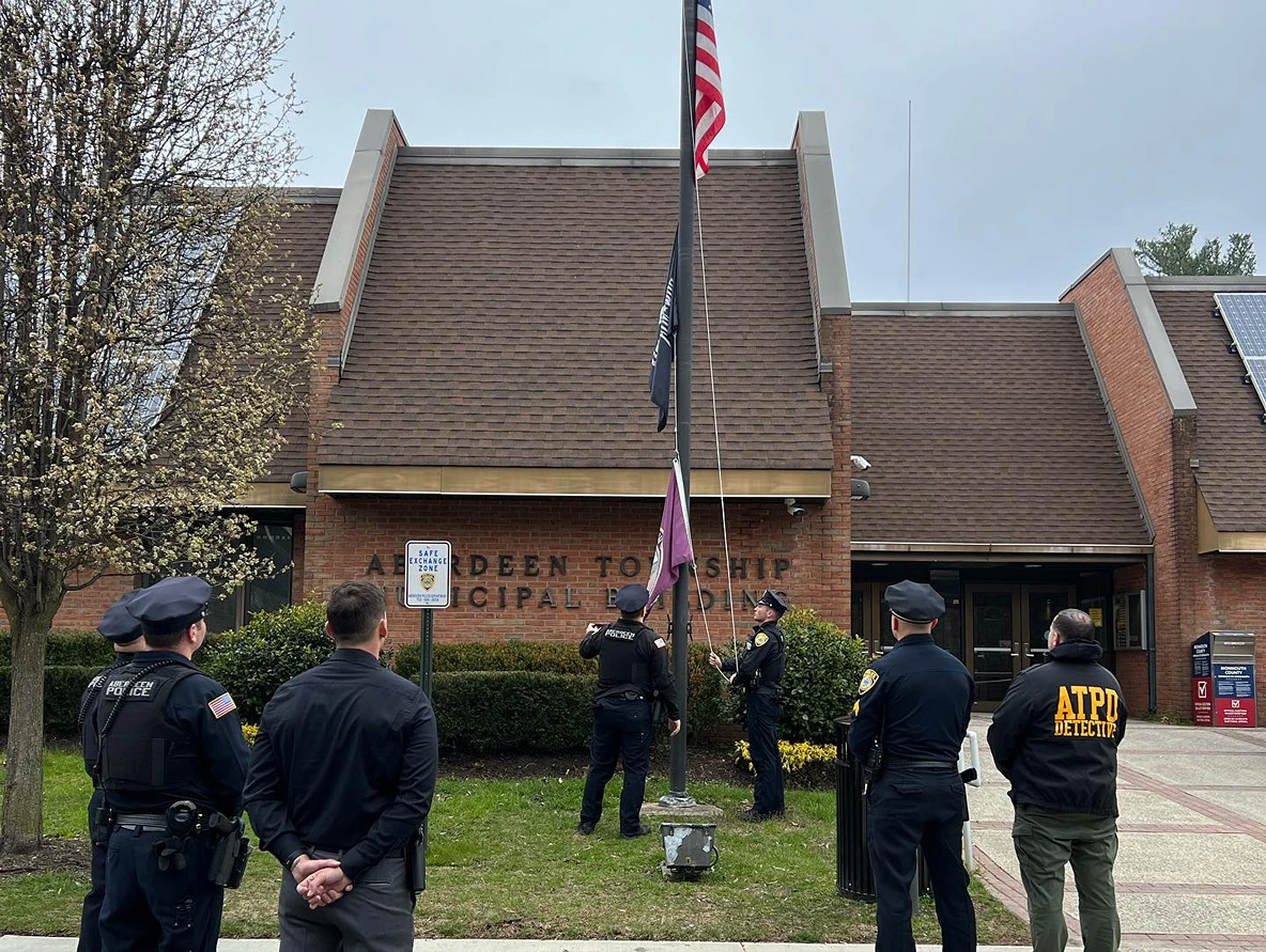 Police officers standing in front of Aberdeen Township Municipal Building while raising flags on a flagpole.