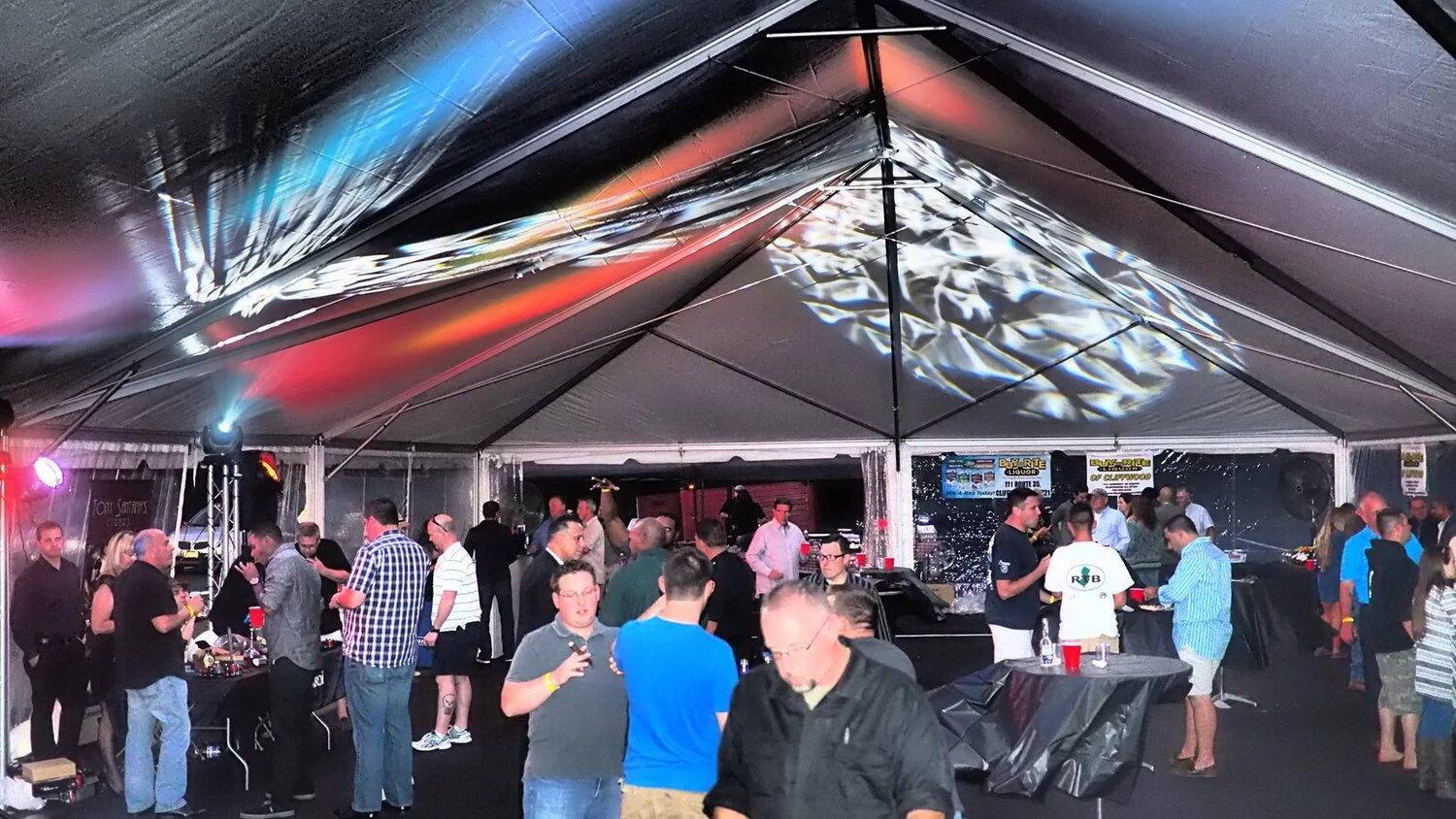 large group of people under a tent with strobing lights 