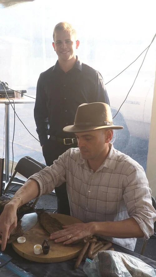 a man at a table making a cigar while another watches from behind