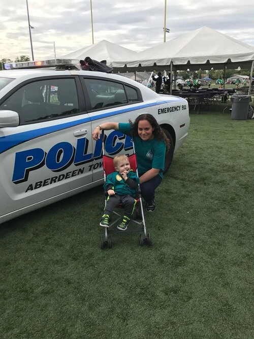 a woman and child in a stroller in front of a police car