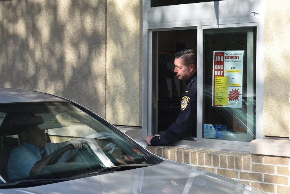 a police officer stands in the drive thru window as a car approaches