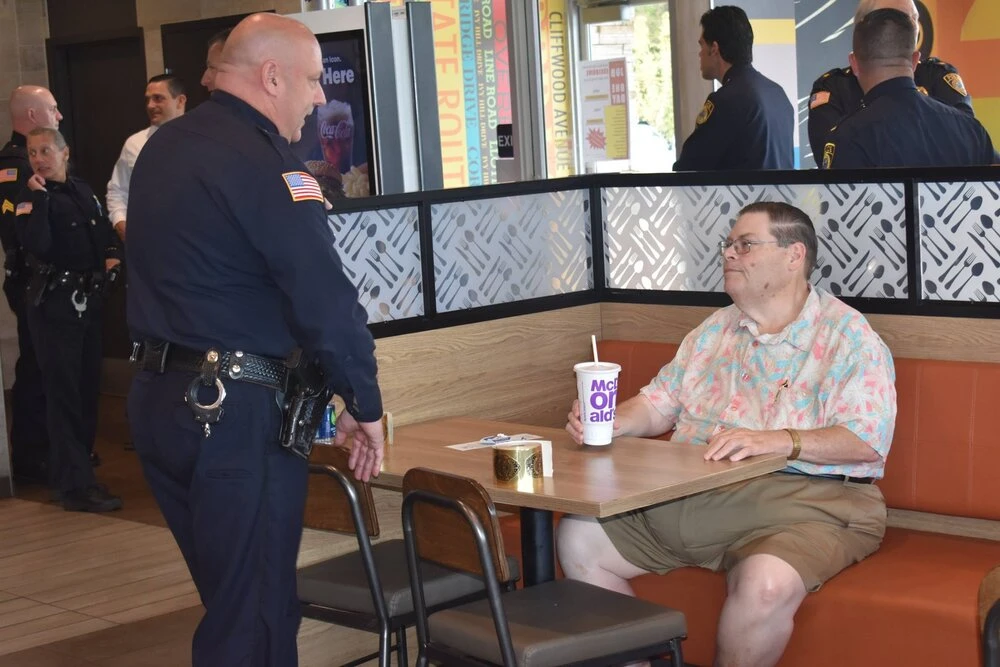 a man sitting at a table speaks with a police officer