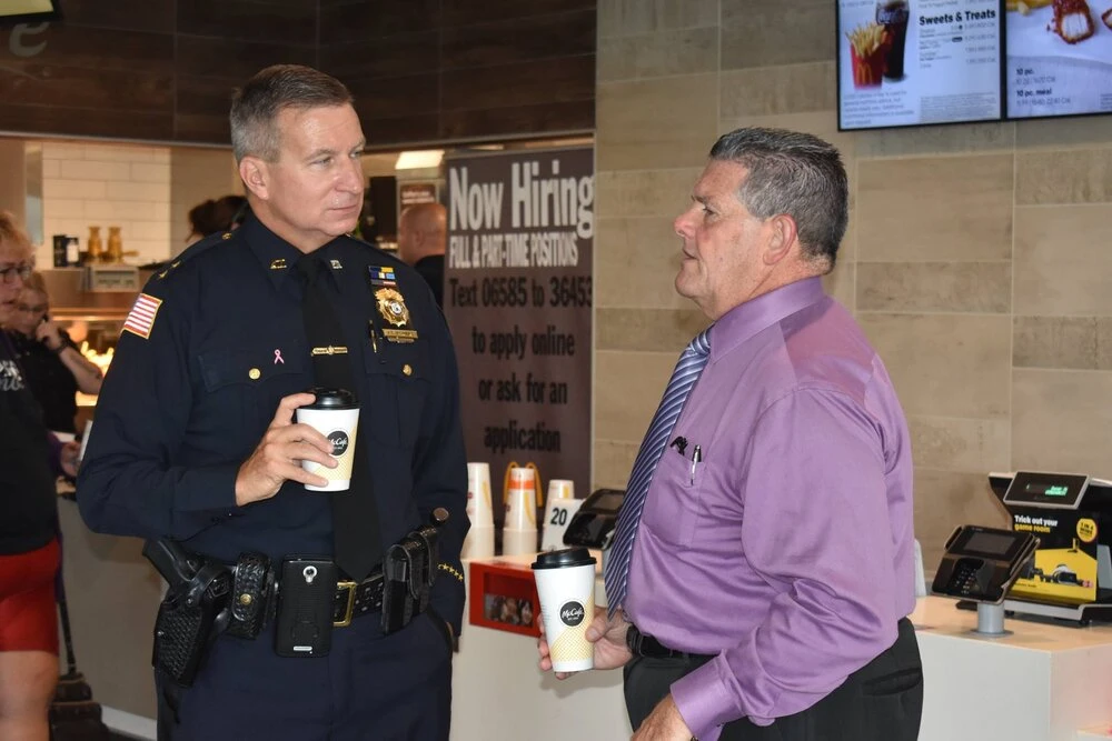 a man speaks with a police officer holding a cup of coffee