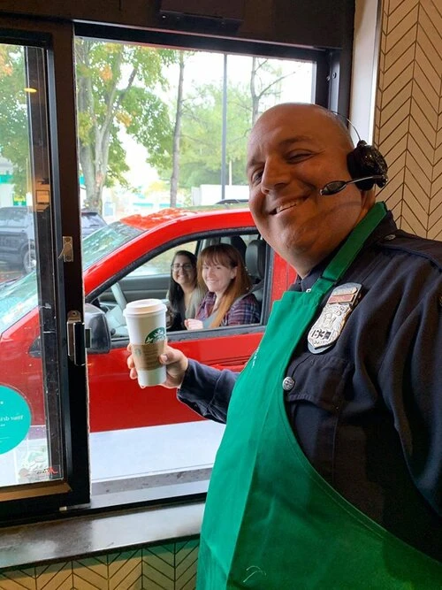 a police officer smiles as he hands coffee to a customer.