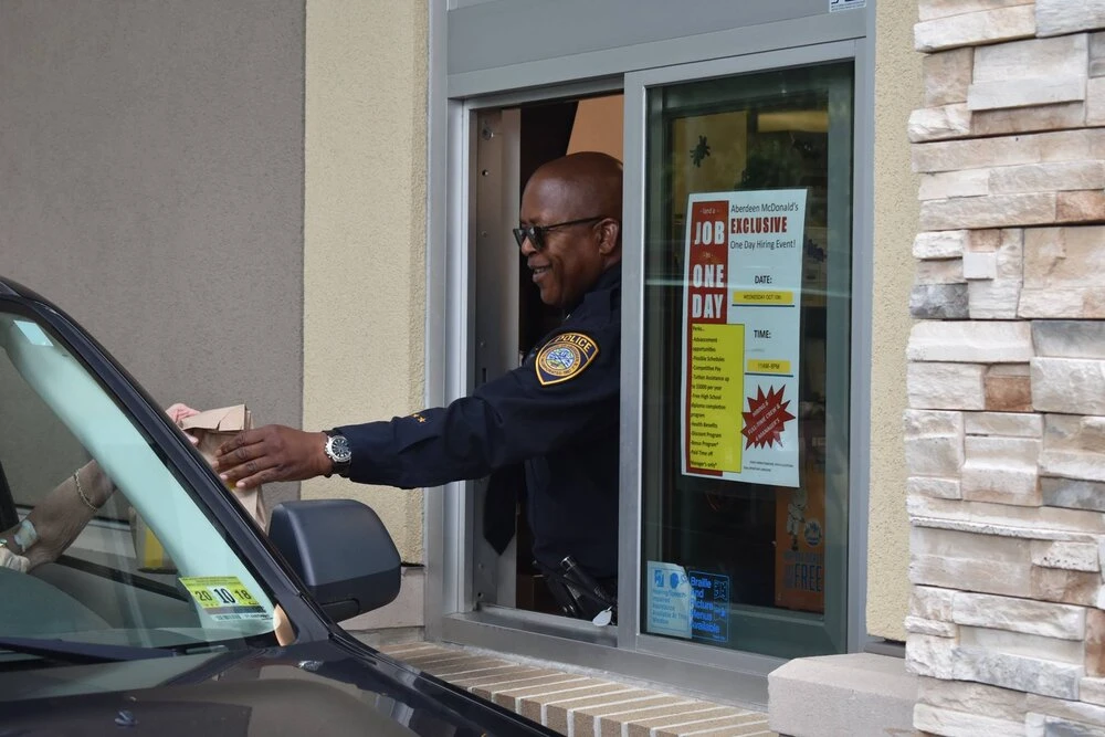 a police officer hands food to a customer in the drive through window