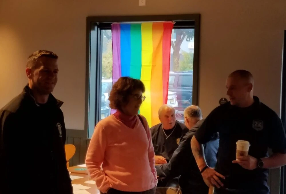 a police officer speaks with a patron while holding a cup of coffee