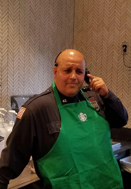 a police officer in a green starbucks apron uses his headset