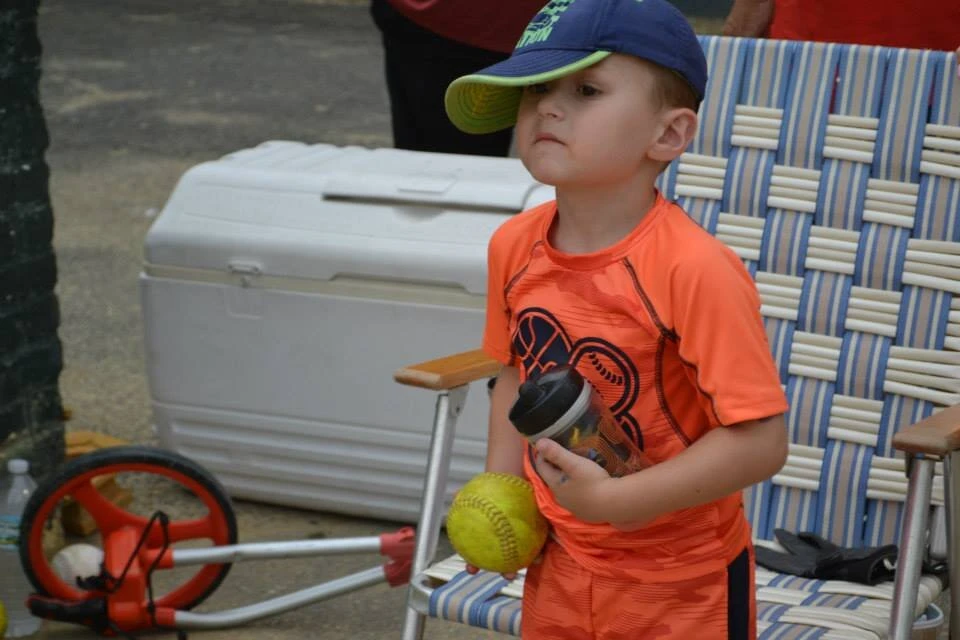 a little boy in a baseball cap holds a ball