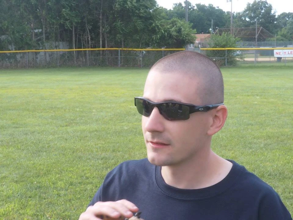 a man wearing sunglasses standing in a baseball field