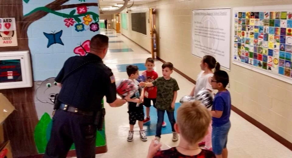 a police officer stands with children holding bicycle helmets