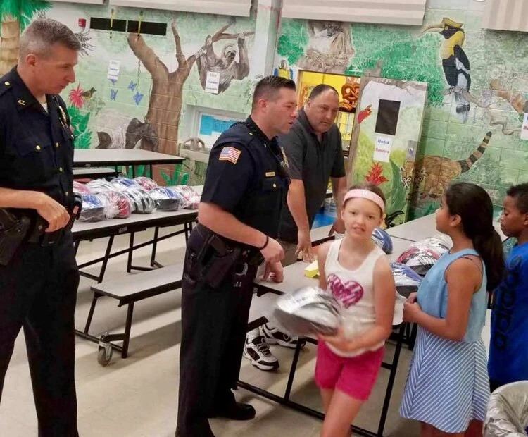a police officer hands out helmets to a line a children