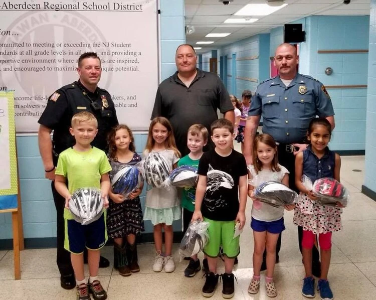 3 police officers stands with children holding bicycle helmets