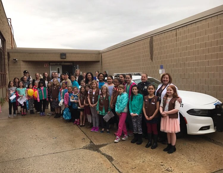 a large group of children and teachers standing in front of a police car