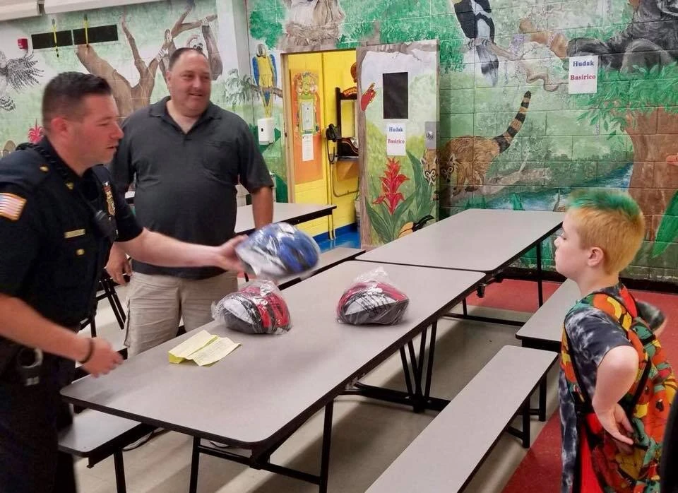 a police officers hands a bicycle helmet to a little boy