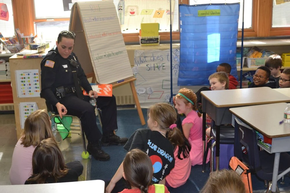 a police officer points to something as children sit around her listening
