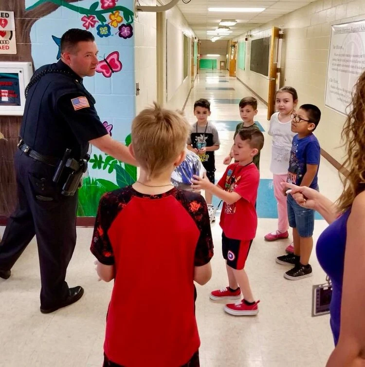 a police officer stands with children holding bicycle helmets