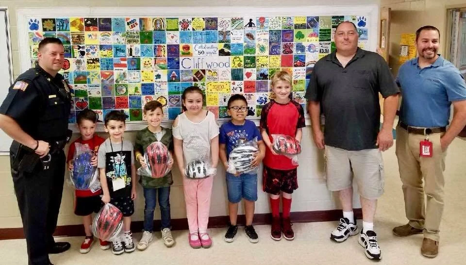a police officer stands with children holding bicycle helmets