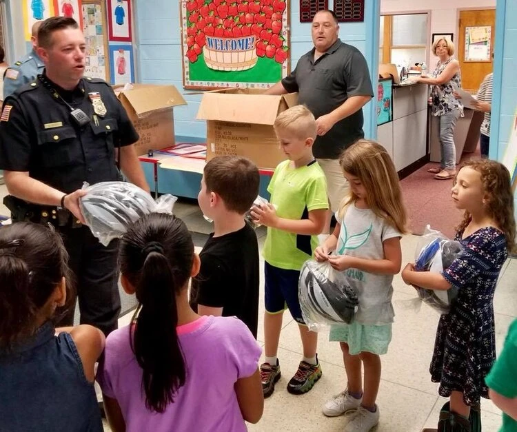 a police officer hands out helmets to a group of children