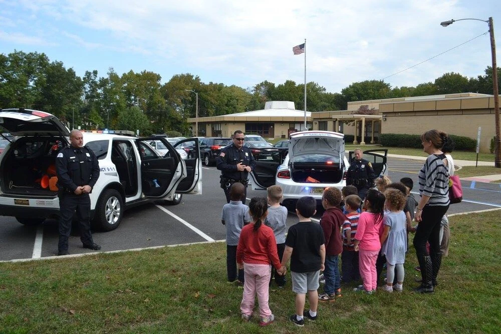 a row of parked police cars with children standing around them