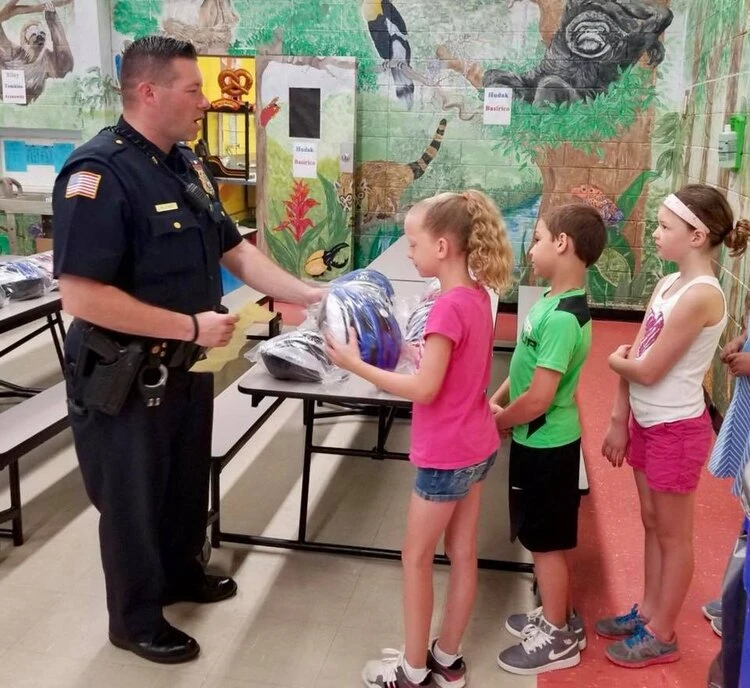 a police officer hands out helmets to a line a children