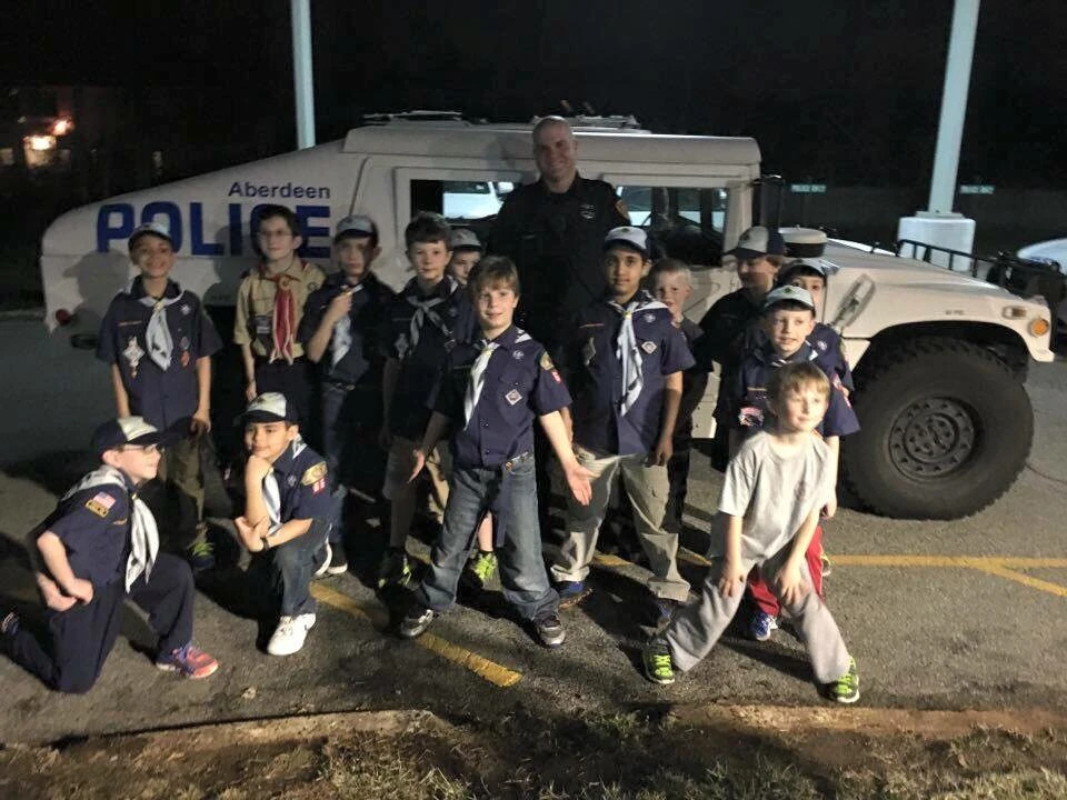 a police officer and a group of children stand in front of a police truck at night