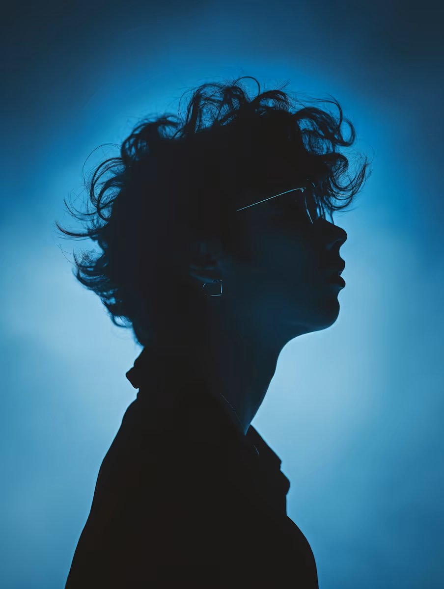 Silhouette of a person with curly hair and glasses against a blue glowing background.