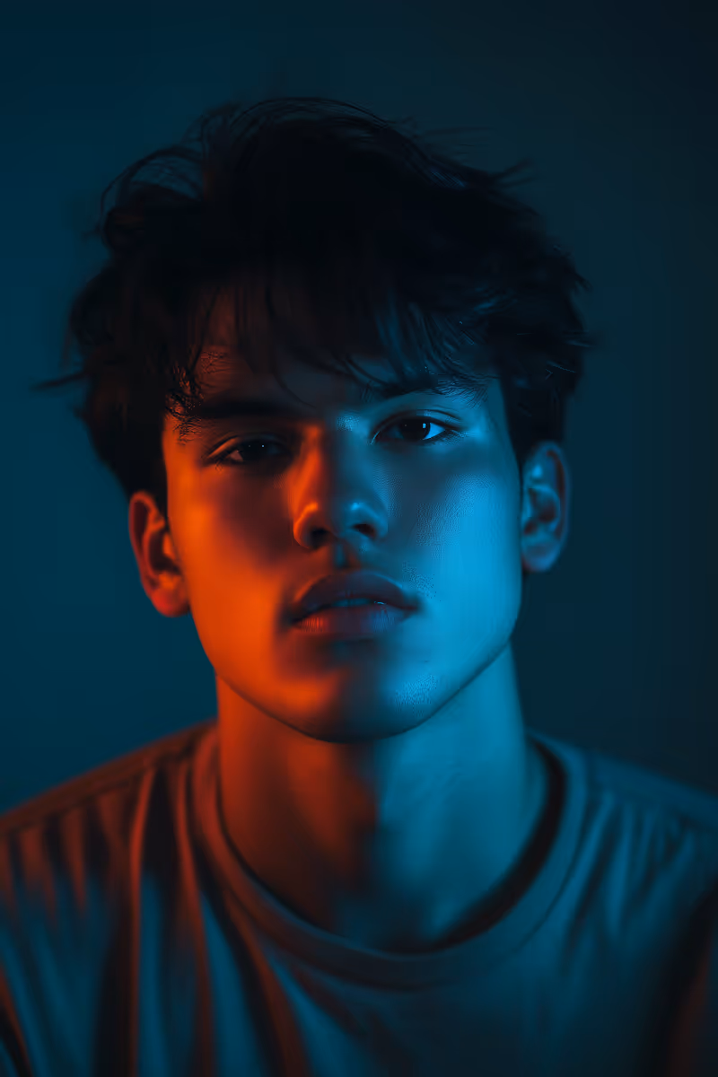 Close-up portrait of a young man with blue and orange lighting on his face against a dark background.