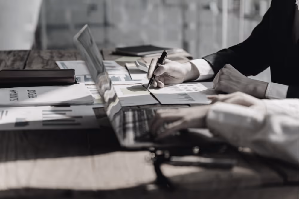 People working on laptop and analyzing business reports with charts and data on a wooden table.