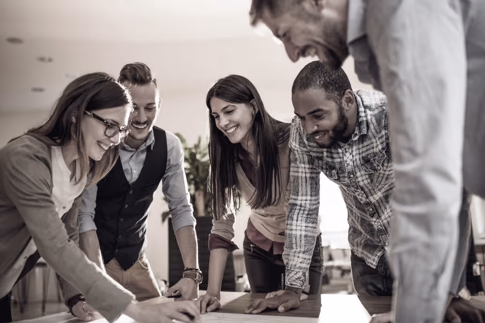 Five diverse colleagues gathered around a table, smiling and engaged in a collaborative discussion.