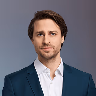 Headshot of a Robert Oppenheim with short brown hair wearing a white shirt and dark blazer against a gray background.