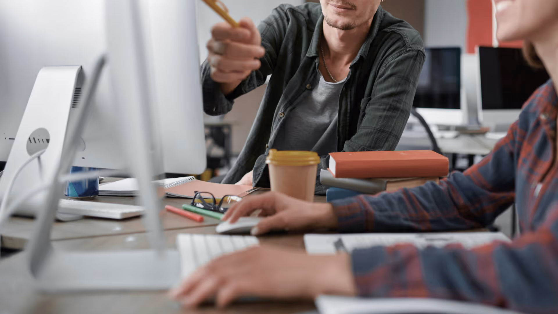 Two people working together at a computer in an office, one pointing at the screen and the other using the mouse.