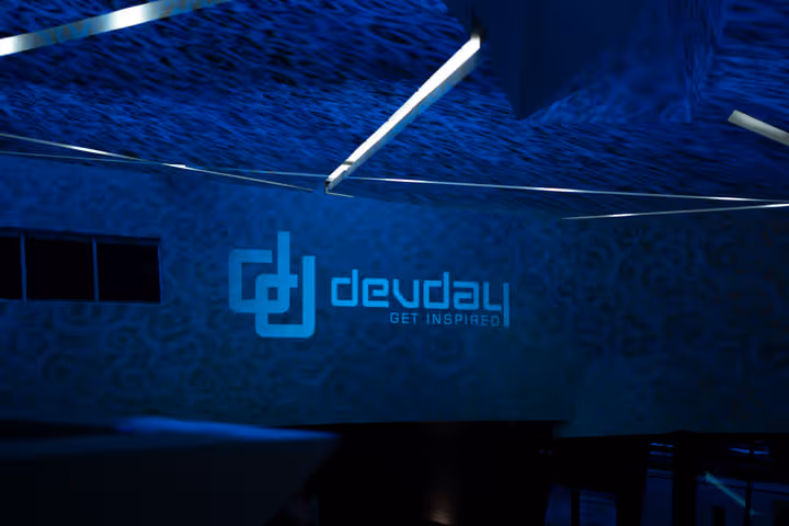 Logo bleu lumineux de 'devday' avec le slogan 'GET INSPIRED' sur un mur sombre dans une salle faiblement éclairée.
