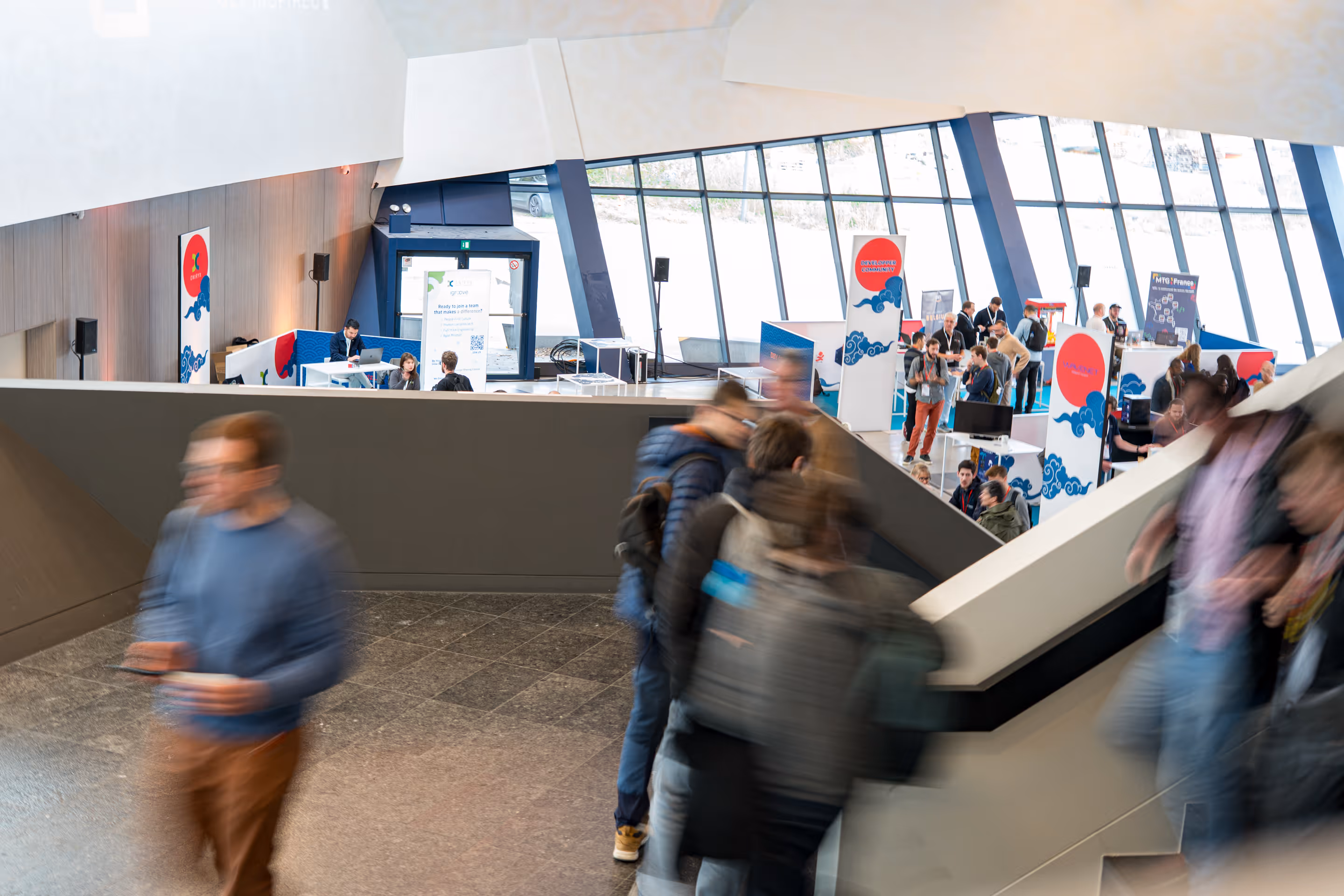 Personnes animées se déplaçant dans un espace d'exposition moderne avec des stands et des vitrines.