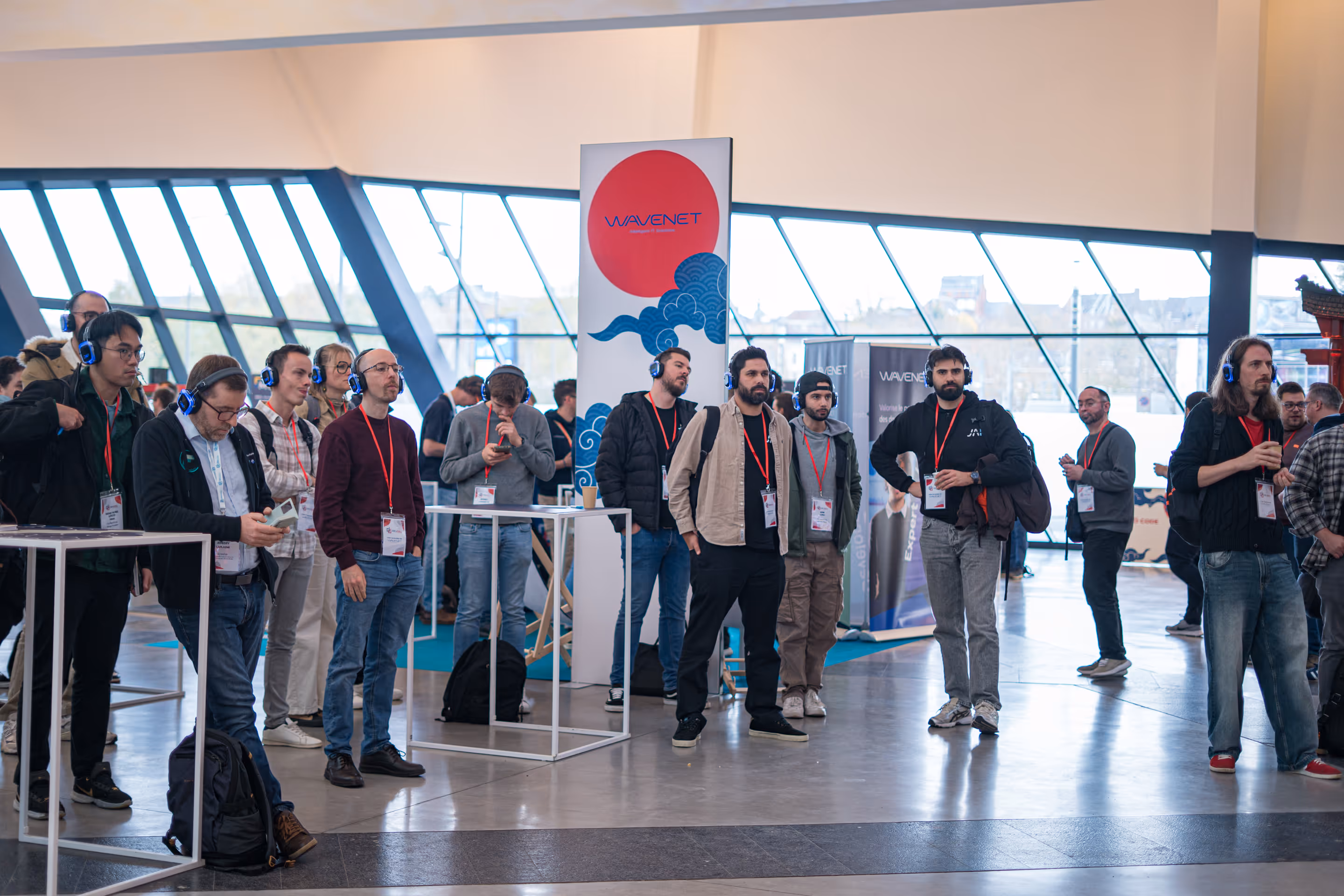 Un groupe de personnes avec des casques bleus écoute une présentation lors d'un événement en intérieur près d'un panneau Wavenet.