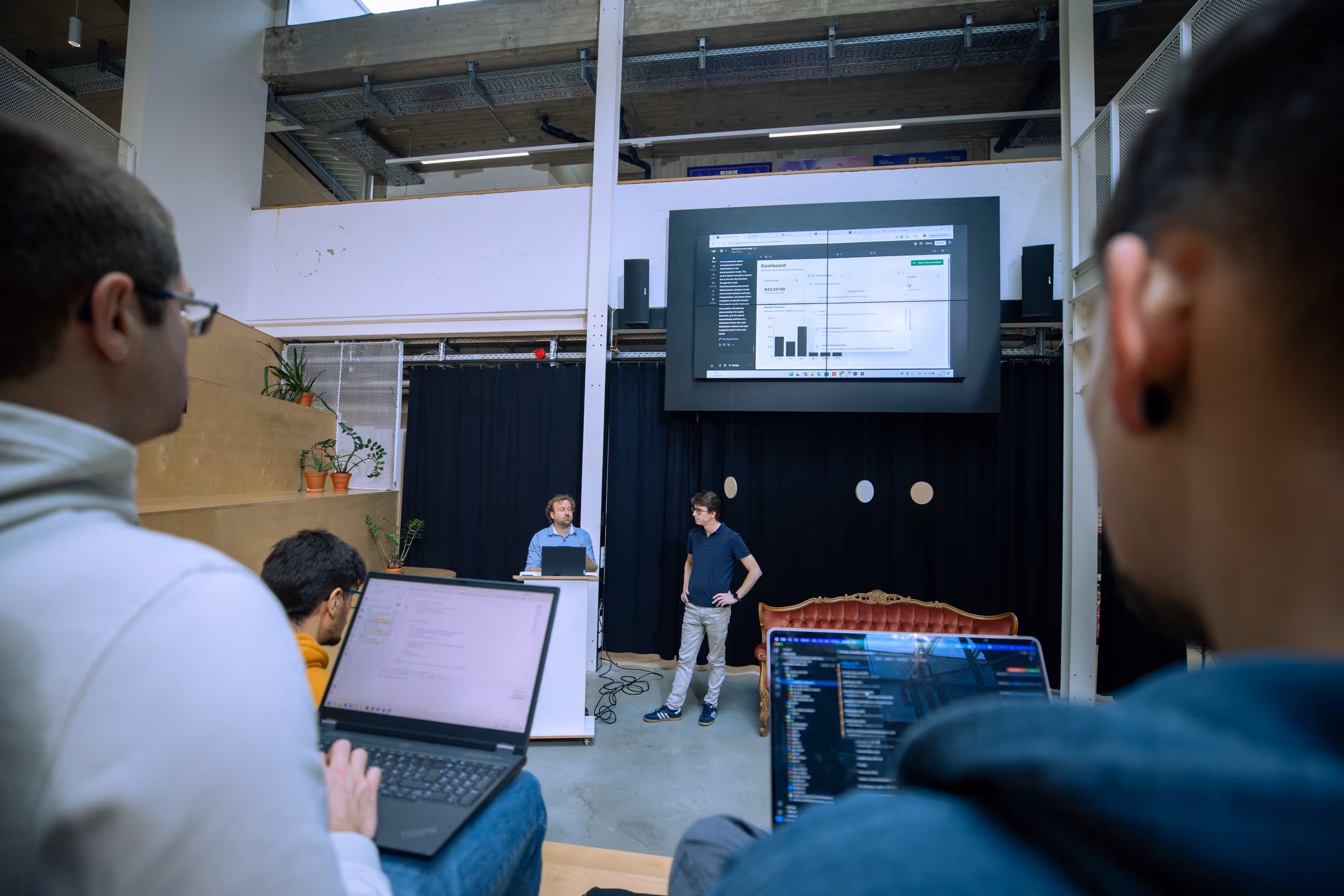 Des collègues assistent à une présentation dans un espace de travail avec un écran affichant un tableau de bord financier.