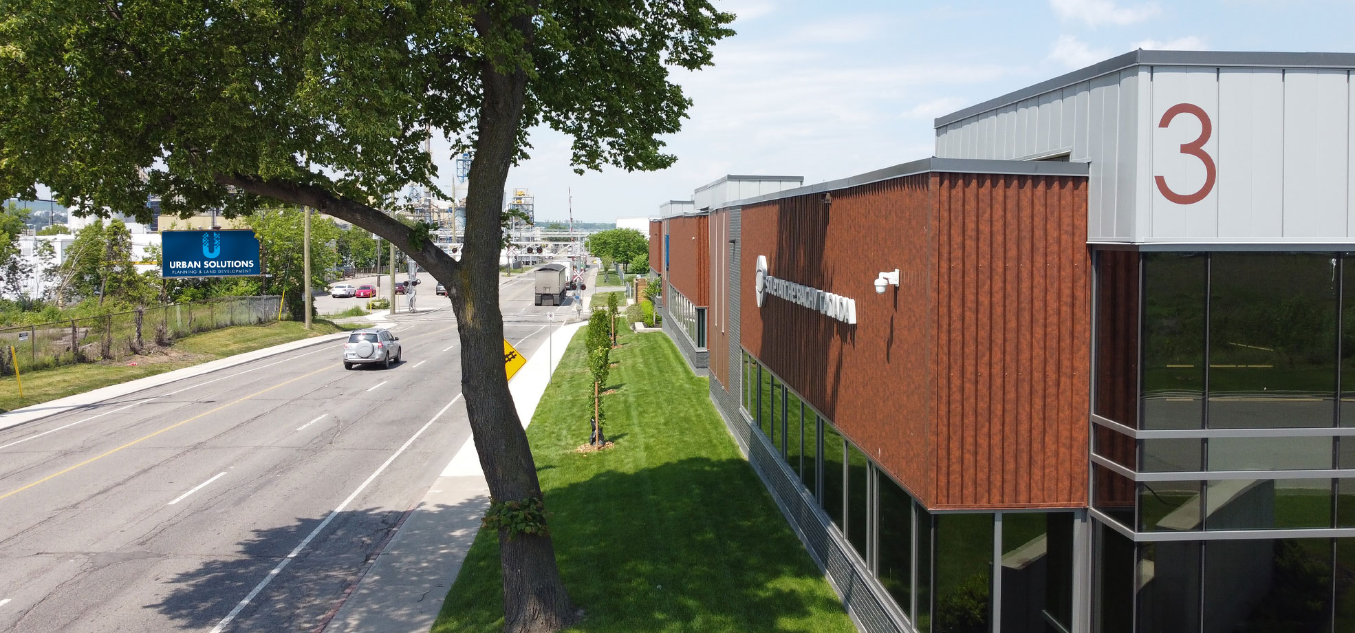 Modern commercial building with wood-toned exterior and large windows along a city street, featuring Urban Solutions signage and landscaped green space.