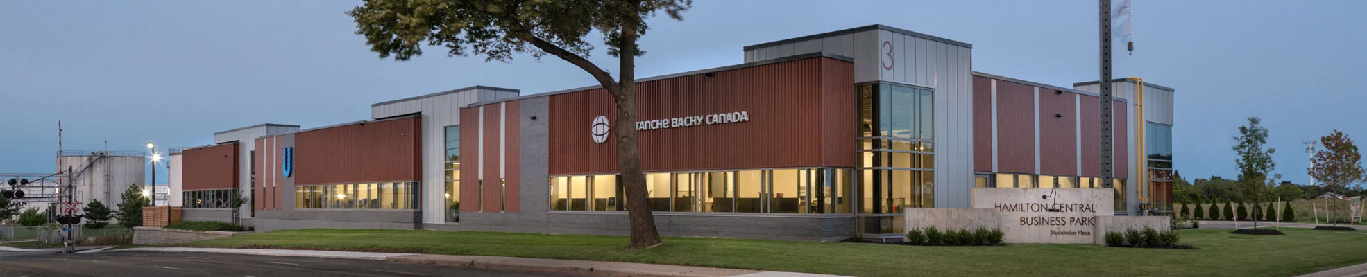 Wide exterior view of a modern commercial building at Hamilton Central Business Park with illuminated offices, landscaped lawn, and street frontage at dusk.
