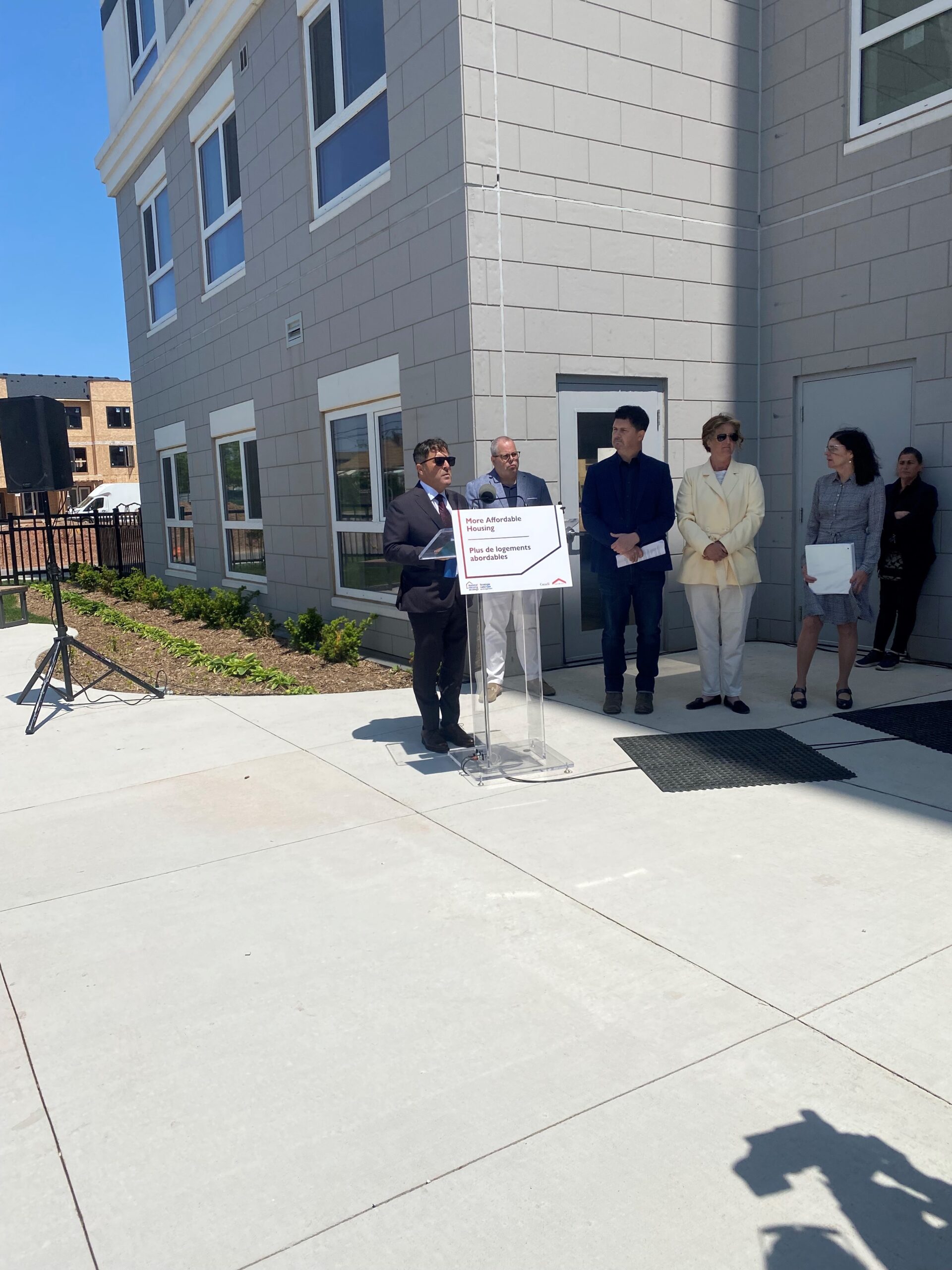 Officials stand at a podium outside 8 Roxanne Drive during a ribbon-cutting ceremony, speaking about new affordable housing.
