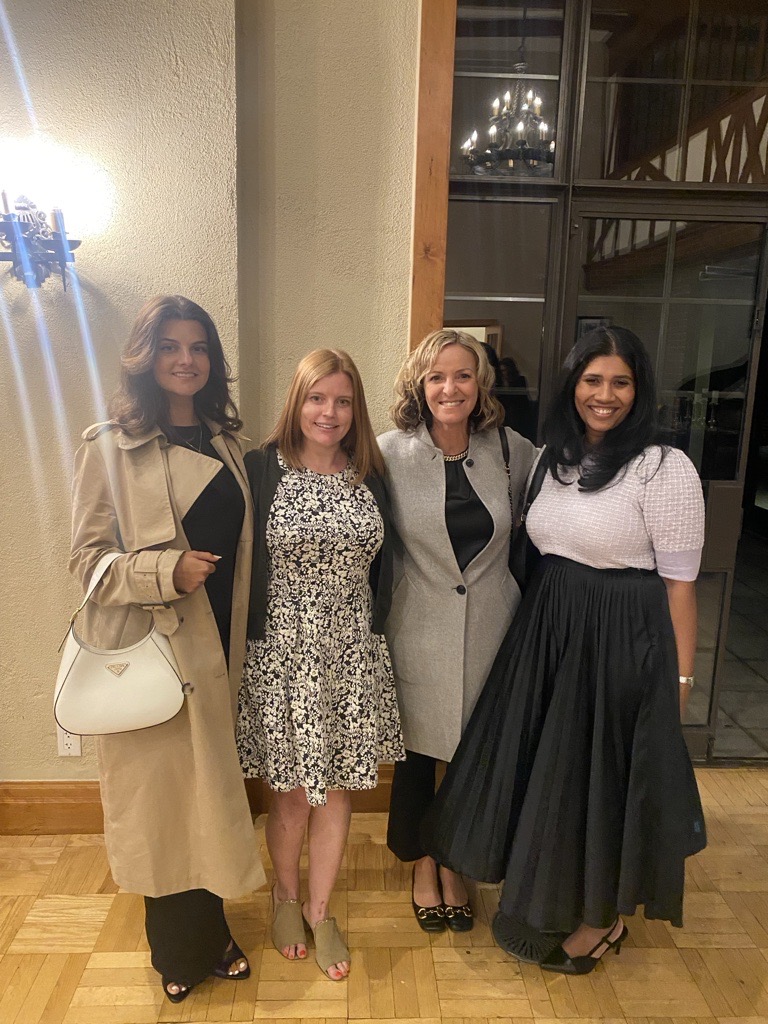 Four women dressed in semi-formal attire stand together and smile at the UrbanSolutions 10-year celebration event.