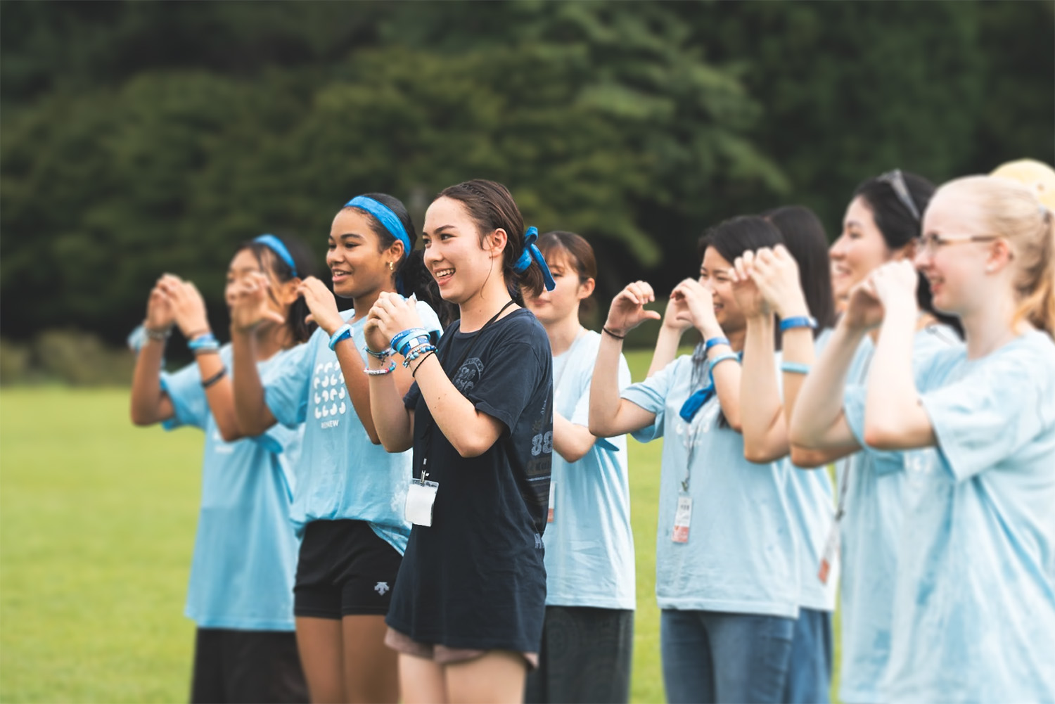 Group of young women standing outdoors in a line, smiling and forming heart shapes with their hands.