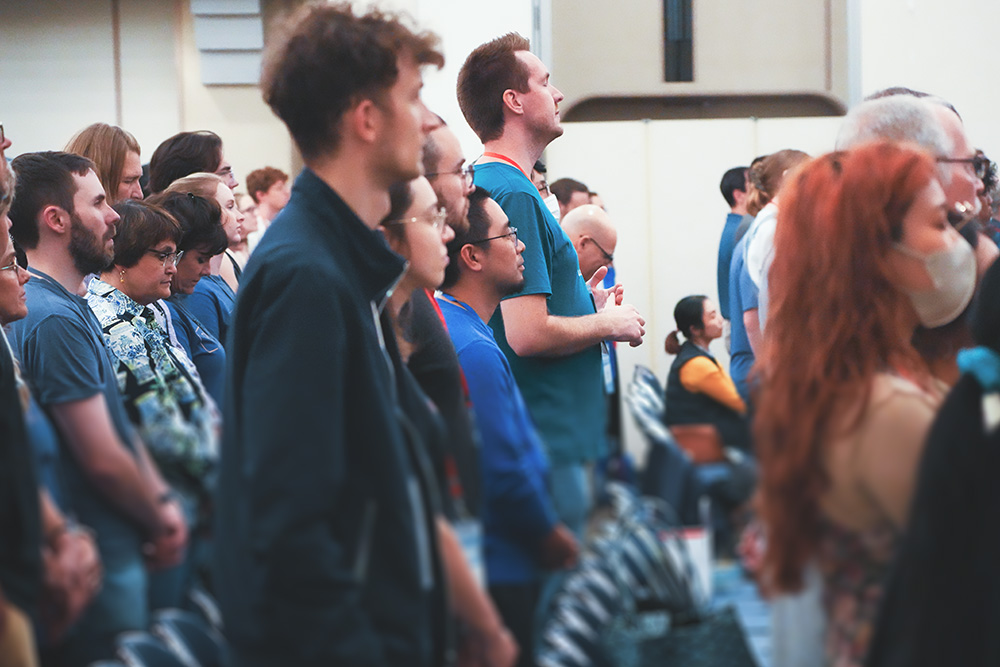 Diverse group of people standing and attentively listening in a conference or seminar setting.
