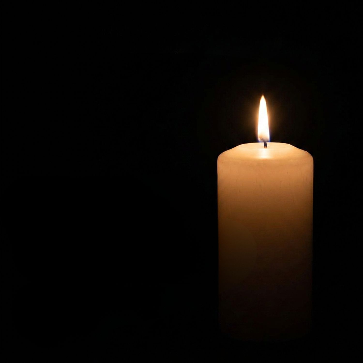 A single lit white candle glowing softly against a black background.