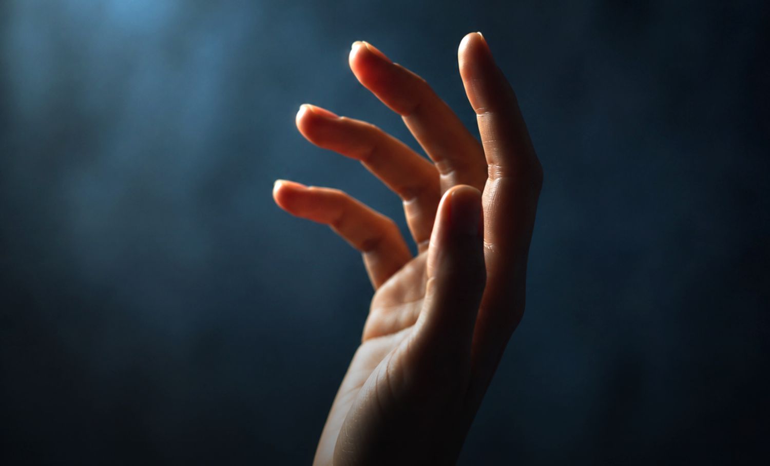 Close-up of a hand with fingers slightly spread against a dark, blurry background.