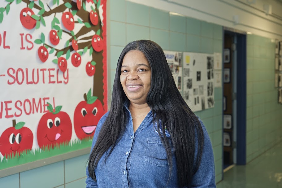 Ms. Martinez smiling in a school hallway near apple bulletin board