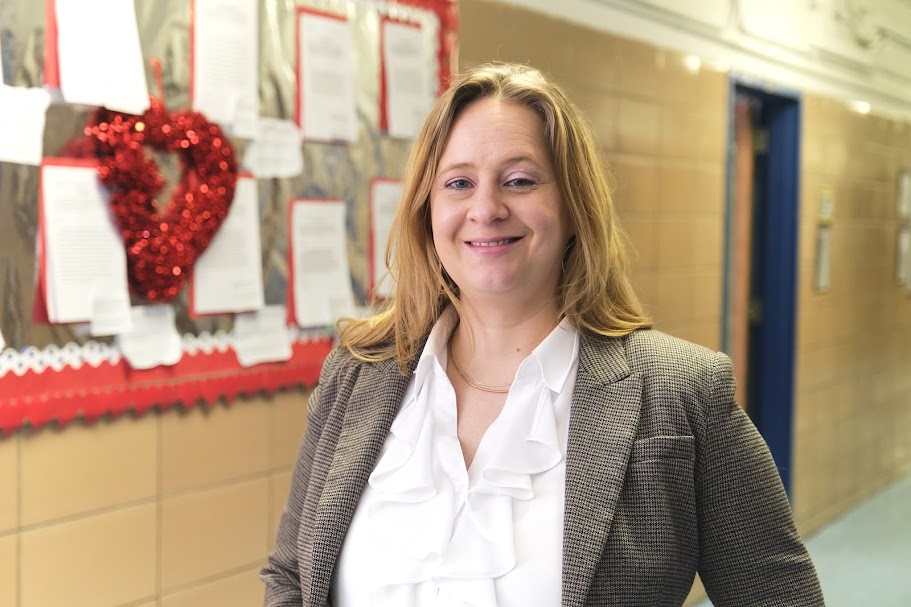 Ms. Hamson smiling in a school hallway near bulletin board